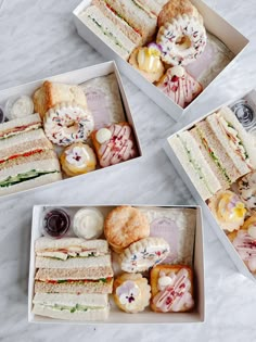 four boxes filled with sandwiches and pastries on top of a white marble countertop