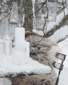 candles are lit in the snow on an outdoor table with fur and glass jars hanging from it