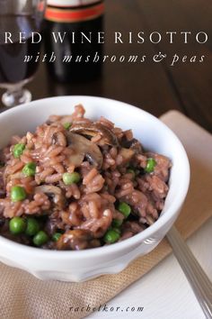 a white bowl filled with rice and peas next to a glass of wine on top of a table