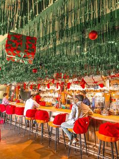 people are sitting at the bar with red and green decorations hanging from the ceiling above them