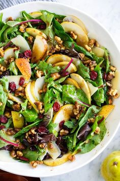 a salad with apples, pears and cranberries in a white bowl on a marble table