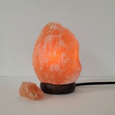 an orange himalayan salt lamp sitting on top of a wooden stand next to a rock