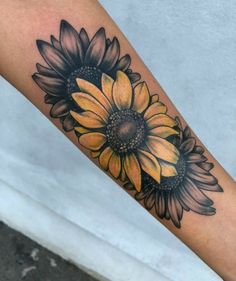 a sunflower tattoo on the arm with black and yellow flowers in it's center