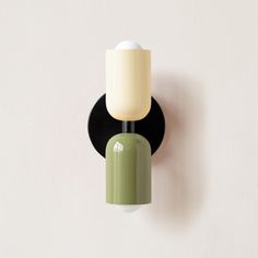 a green and white wall light mounted on the side of a wall next to a black holder