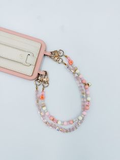 Marigold is a charming and playful accessory to keep your phone secure in style. This handmade wristlet features soft pastel beads, accented with delicate floral details and gold hardware for a touch of elegance. Lightweight and easy to carry, the Marigold wristlet is perfect for adding a pop of color to your day while keeping your phone close at hand. Whether you're out running errands or dressing up for an occasion, this wristlet combines function and fashion effortlessly. Chain: The beaded wr