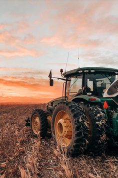 a tractor is parked in the middle of a field at sunset, with its lights on