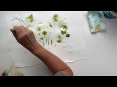 an older woman is painting flowers on a piece of paper