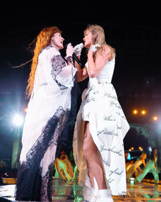 two women in white dresses on stage with one holding her hand out to the other