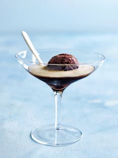 an ice cream sundae in a glass bowl on a blue surface with a spoon