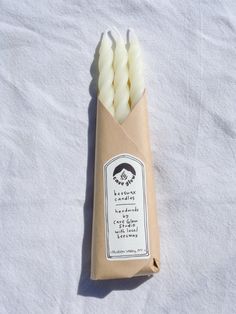 four white candles are in a tube wrapped in brown paper on a white sheeted surface