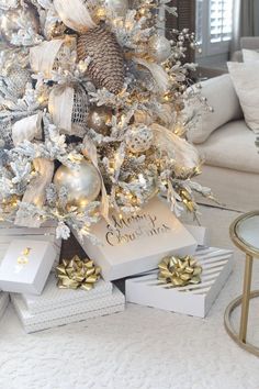 a white christmas tree with gold and silver ornaments on it, surrounded by gifts in boxes