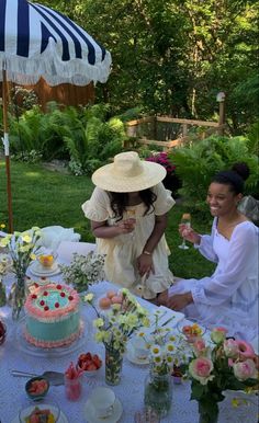 two women are sitting at a table with cake and flowers on it while one woman holds an umbrella over her head