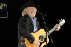 a man with a cowboy hat singing into a microphone and holding a guitar in his right hand