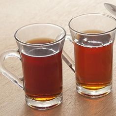 two mugs filled with tea sitting on top of a wooden table next to each other