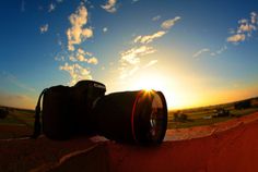 two cameras sitting on top of a red wall with the sun setting in the background