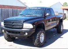 a black dodge ram truck parked in front of a wooden fence and building with red trim