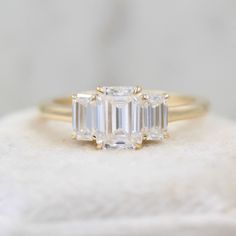 an emerald cut diamond engagement ring with three baguettes on top, set in yellow gold