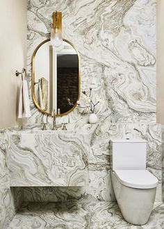 a white toilet sitting next to a sink in a bathroom under a large round mirror