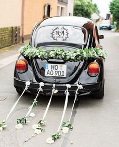 a black car with white flowers tied to it's trunk and the back door