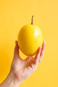 a hand holding an orange against a yellow background