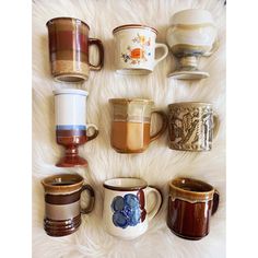 there are many coffee mugs lined up on the fur surface, all different colors and sizes