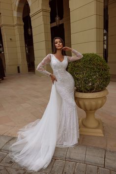 a woman in a wedding dress standing next to a potted plant and posing for the camera