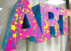 the word art is painted bright pink and blue with yellow splatters on it