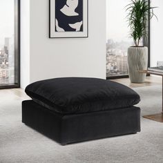 a black ottoman sitting on top of a white carpeted floor next to a window