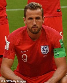 a man sitting on top of a soccer field wearing a red shirt and blue shorts