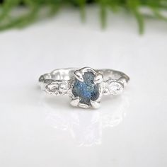 a white gold ring with a blue diamond in the center and leaves on the side