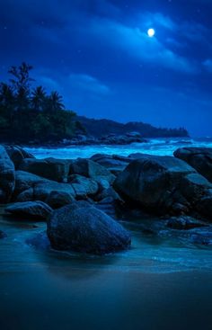 the moon is setting over some rocks on the beach