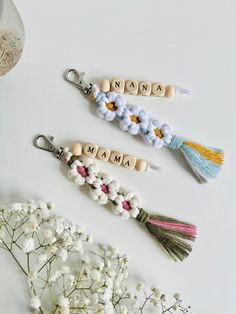 three wooden name keychains with tassels on them and flowers in the background