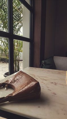 a brown purse sitting on top of a table next to a window