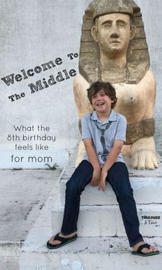 a young boy sitting in front of a statue with the words welcome to the middle