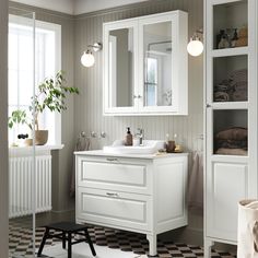 a white bathroom with black and white checkered flooring on the floor, two mirrors above the sink