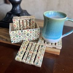 a cup of tea sits next to some matchsticks on a wooden table with a lamp in the background