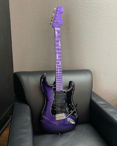 a purple electric guitar sitting on top of a black leather chair next to a wall