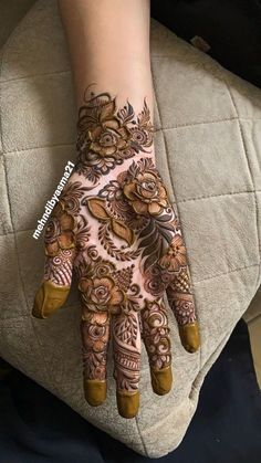 a woman's hand with hennap and flowers painted on it, sitting on top of a cushion