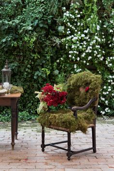 a chair covered in moss sitting next to a table with flowers on top of it