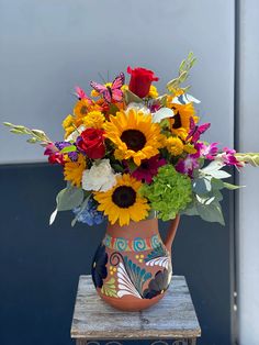 a vase filled with lots of colorful flowers on top of a wooden table next to a wall