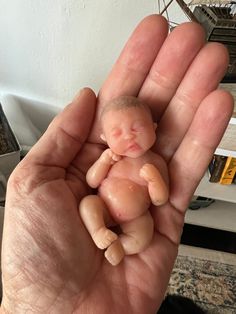 a hand holding a tiny baby doll in it's palm