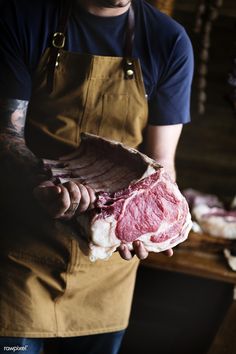 a man holding a piece of raw meat in his right hand and wearing an apron