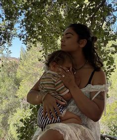 a woman holding a baby under a tree