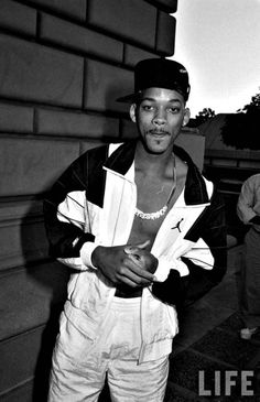 a black and white photo of a man standing in front of a building with his hands on his hips