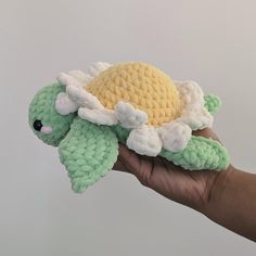 a hand holding a crocheted stuffed animal in the shape of a turtle with wings