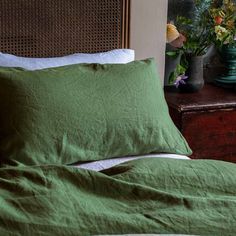 a bed with green sheets and pillows on top of it next to a wooden dresser