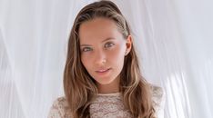 a woman with long hair and blue eyes is posing for a photo in front of a white curtain