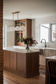 an instagramted photo of a kitchen with wooden cabinets and white counter tops, along with flowers in a vase on the island