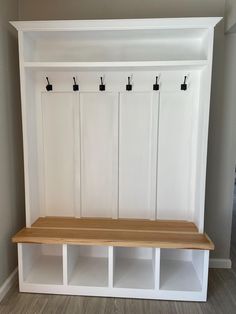 a white bench with three hooks on the back and two cubbys underneath it