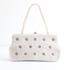 This darling 1950's full beaded handbag with rhinestone accents, is the perfect statement accessory.  The rectangular shape of the bag boasts an ivory bead covered base in a rippled design and claw set rhinestone accents surrounded by grey bugle beads that set off the silver toned metal kiss lock clasp. This is framed by a fully embellished ivory bead handle. The bag opens to a cream rayon satin lining, with one side pocket and a small mirror.  Measurements Height of Bag: 4.2 inches Length: 8 in Embellished Cream Bags For Events, Embellished Cream Evening Bag, Vintage Beaded Beige Bags, Vintage Embellished Rectangular Bag, Cream Evening Bags With Pearl Embroidery, Handheld Beaded Beige Evening Bag, Beige Beaded Handheld Evening Bag, Vintage White Embellished Bags, Evening Beige Embellished Shoulder Bag